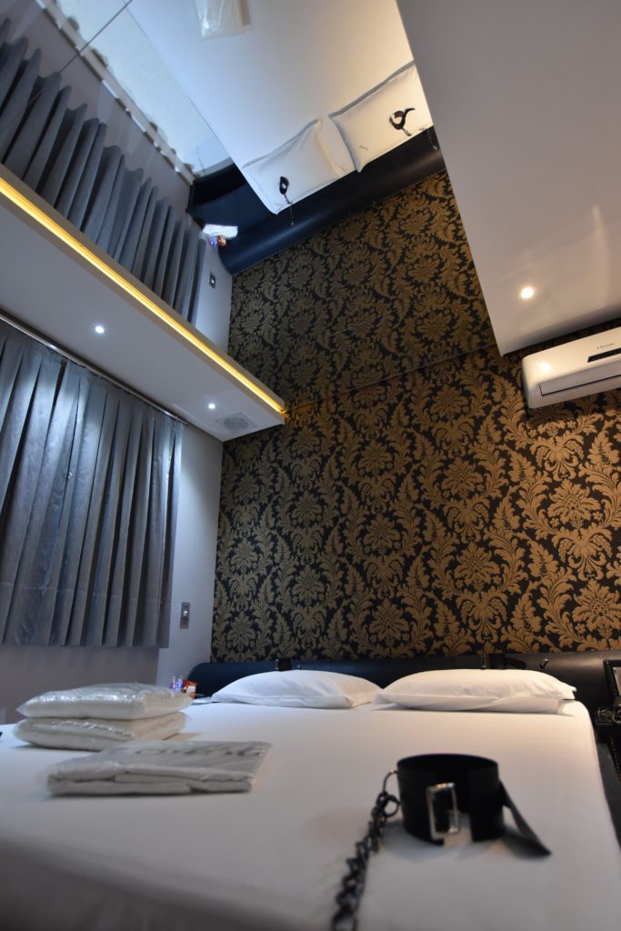 Foto da Suíte Super Luxo 10 do Motel Tarot destacando o espelho sobre a cama com algemas.
