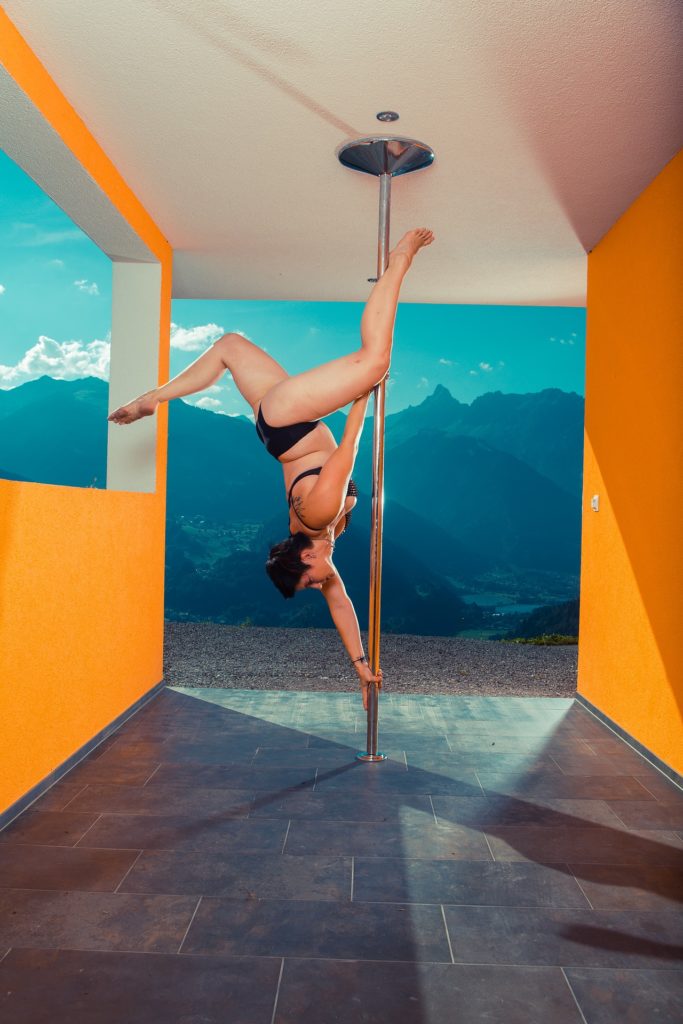 Imagem de uma mulher realizando uma posição de inversão na barra de pole dance.