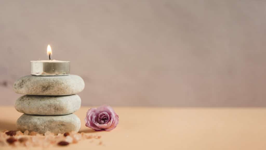 Imagem de vela aromática sobre pedras com uma rosa ao lado.