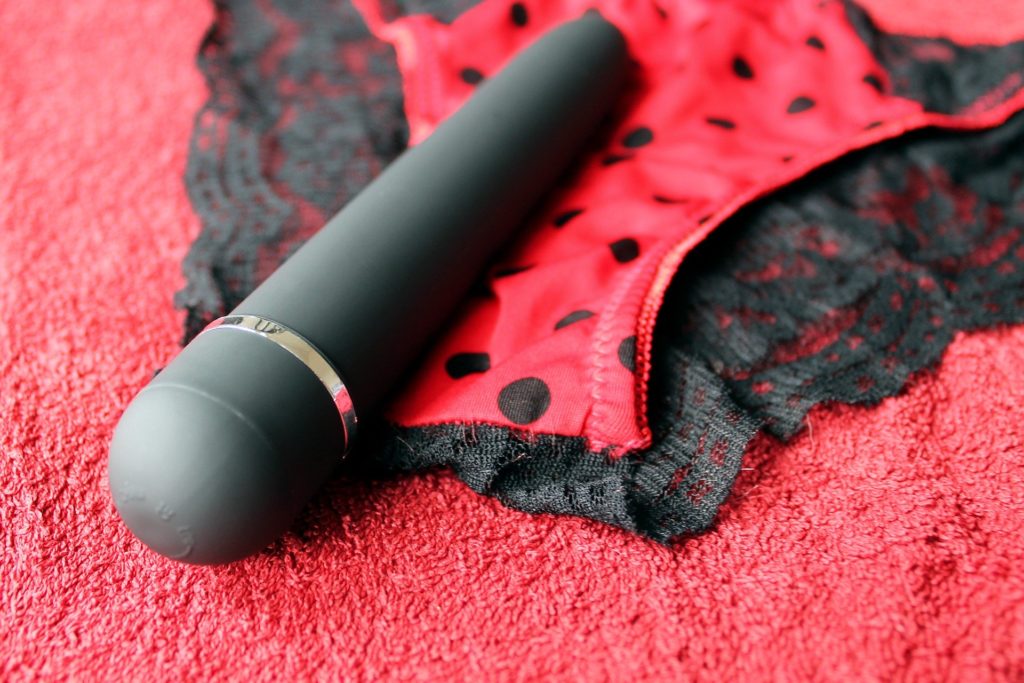 Foto de um vibradror preto discreto sobre calcinha vermelha e preta com renda sexy
